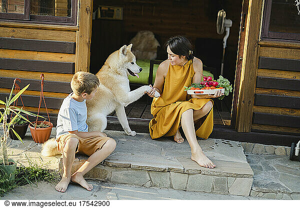 Woman holding vegetable tray shaking hand with dog sitting by son at doorway