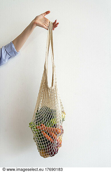 Woman holding vegetables inside mesh bag in front of wall