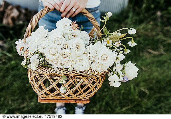 Woman holds woven basket of white roses outside