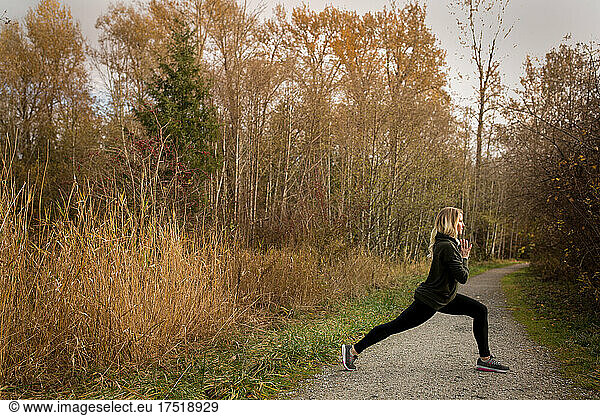 Woman holds yoga pose on trail in autumn