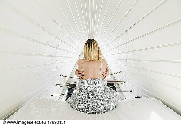 Woman hugging self sitting on bed in attic