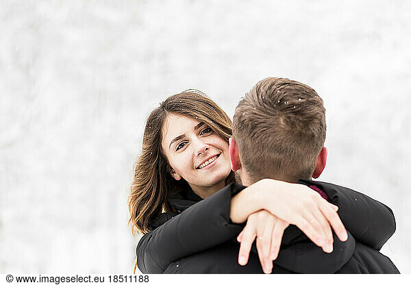 woman hugs her husband's neck in a winter park