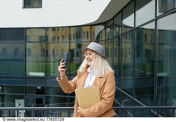 woman in a beige coat communicates on a smartphone holding a notebook