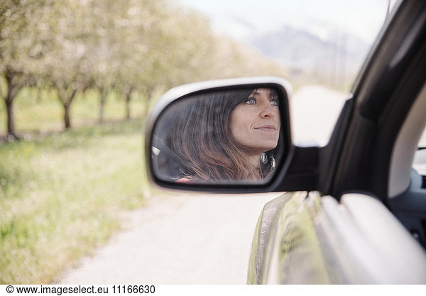Woman in a car on a road trip  reflection seen in the side mirror.