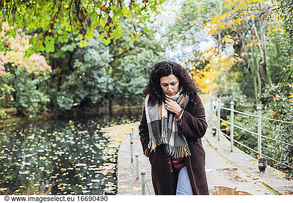 Woman in a coat and scarf looking down  looks sad  walking in a park