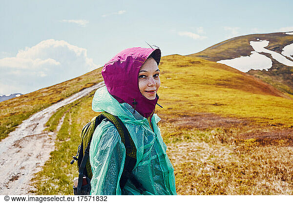 Woman in a raincoat against the backdrop of a mountain peak.