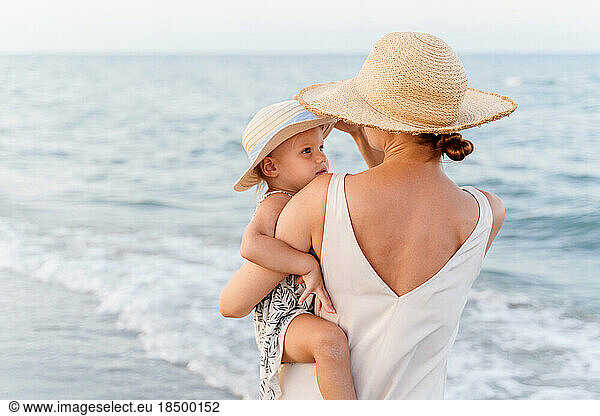 Woman in a straw hat holding a little girl in her arms near the sea