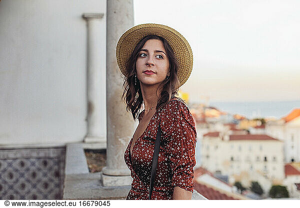 Woman in a straw hat looking aside and smiling  Lisbon sunset view