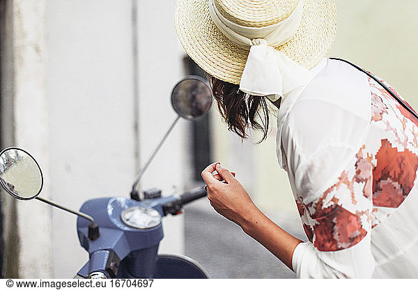 Woman in a straw hat looking at a bike mirror and fixing her makeup