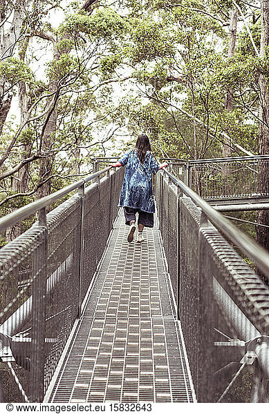 woman in big blue dress climbs along tree top walk in remote australia