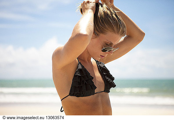 Woman in bikini top adjusting hair at beach