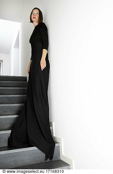 Woman in black dress leaning on wall while standing on staircase
