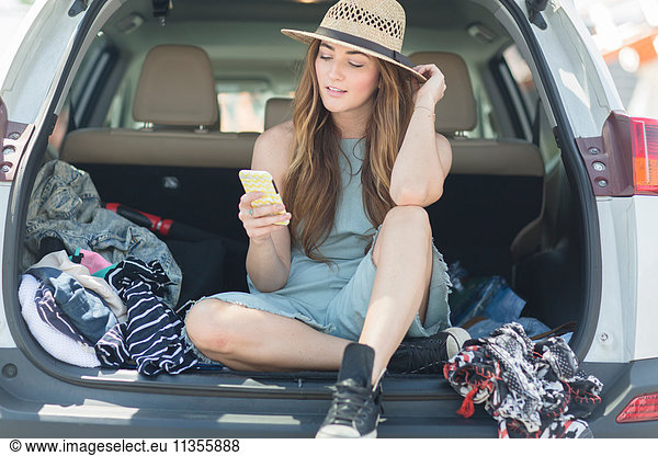 Woman in car boot looking at smartphone