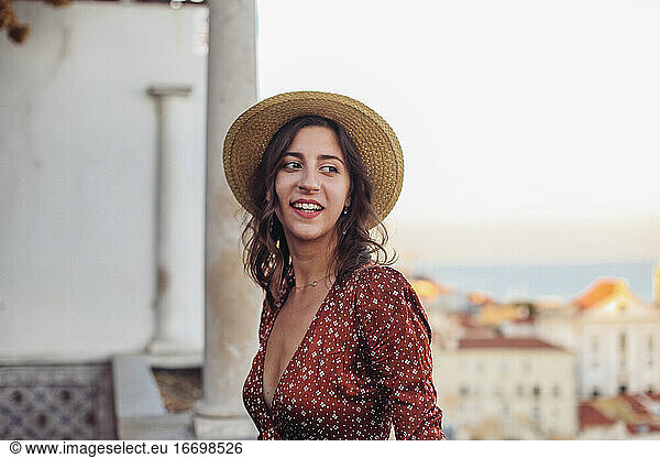 Woman in dress and a straw hat looking over rooftop view of Lisbon