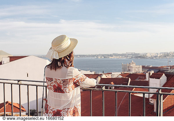 Woman in hat from the back looking over red roofs on Lisbon