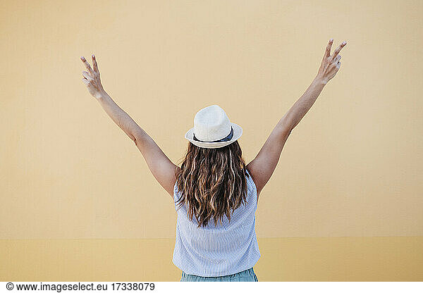 Woman in hat gesturing peace sign while standing in front of brown wall