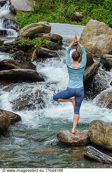 Woman in Hatha yoga balance yoga asana Vrikshasana tree pose at waterfall outdoors