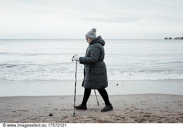 woman in her 70's walking with sticks along the beach in winter
