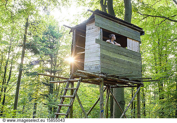 Woman in hunting stand  looking out at forest.