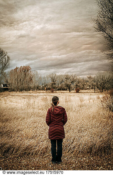 Woman in long down coat in field watches clouds near Taos  NM