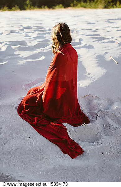 woman in red coat sitting on the sand