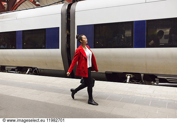 Woman in red coat walking alongside train at station
