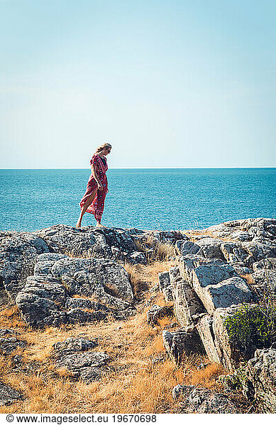 Woman In Red Dress On Rocky Ocean Side In Scandinavia