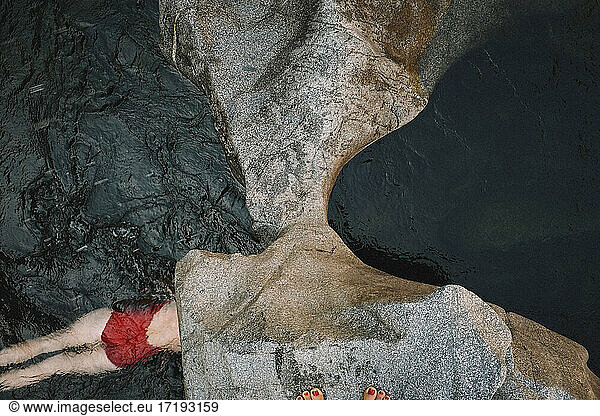 Woman in Red Suit Swims Through Dark Water. View from Above