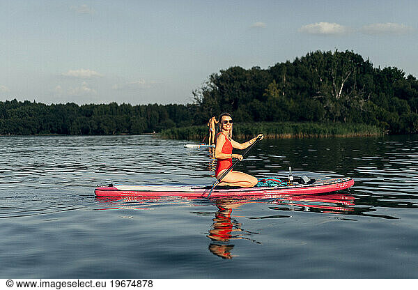 Woman in red swimsuit on paddleboarding on lake on summer. supboard
