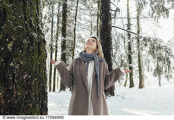 Woman in scarf standing by tree in snow forest