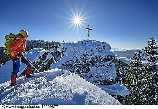 Woman in ski-wear hiking near summit cross on snow covered mountain