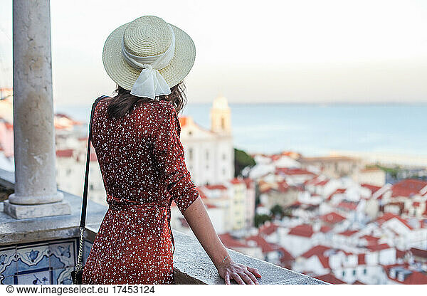 Woman in straw hat and brown dress on a rooftop view point in Lisbon