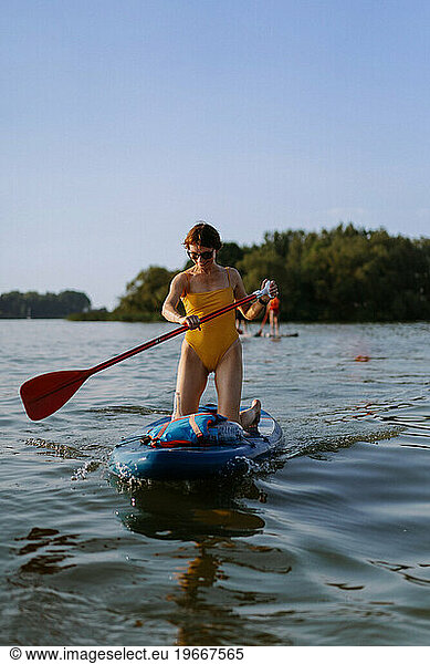 Woman in swimsuit on paddleboard on forest lake in summer. SUP board.
