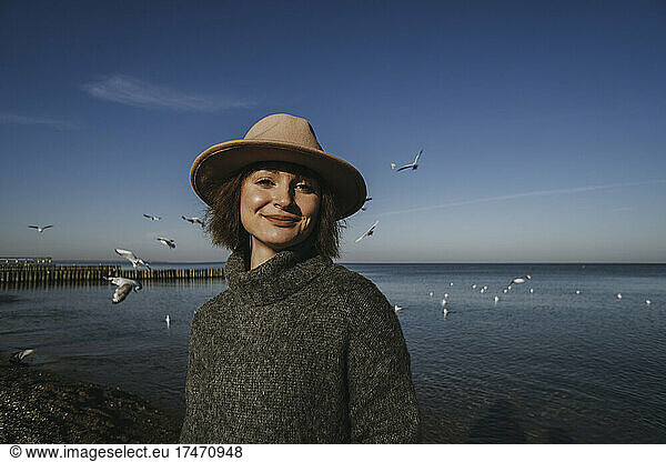 Woman in turtleneck standing at sea in front of blue sky