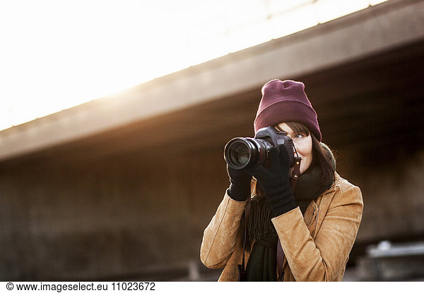 Woman in warm clothing photographing with camera outdoors