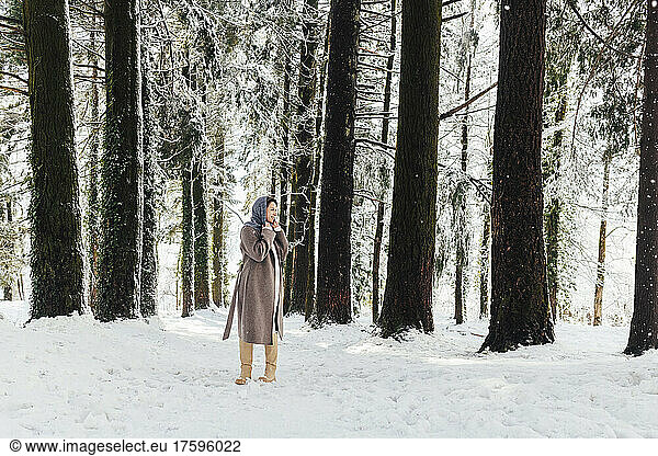 Woman in warm clothing standing in winter forest
