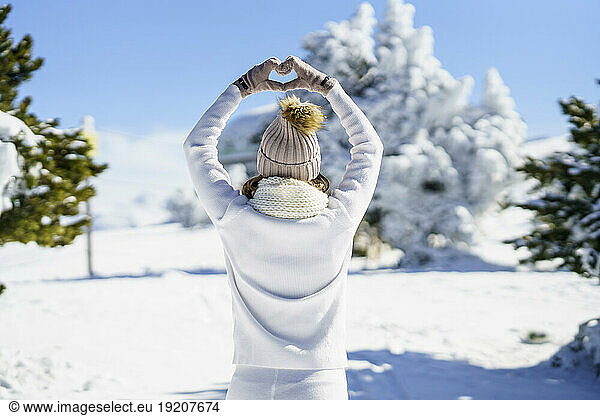 Woman in white outfit making heart shape in winter landscape