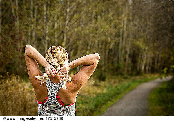 Woman in workout clothes braids hair on trail