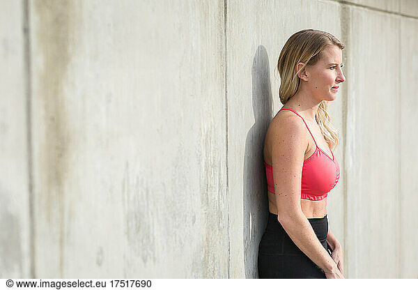 Woman in workout gear relaxes against concrete wall