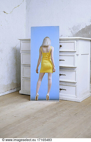 Woman in yellow dress standing while seen in mirror reflection
