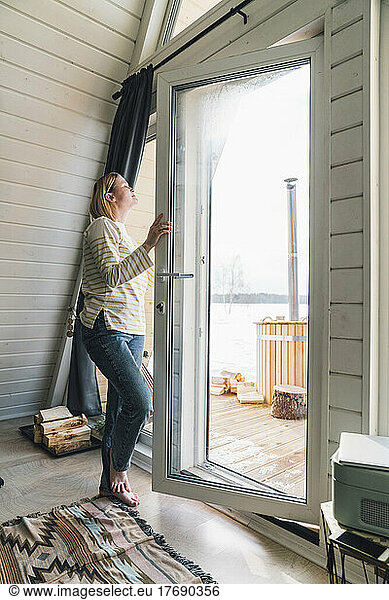 Woman inhaling fresh air opening glass door at home