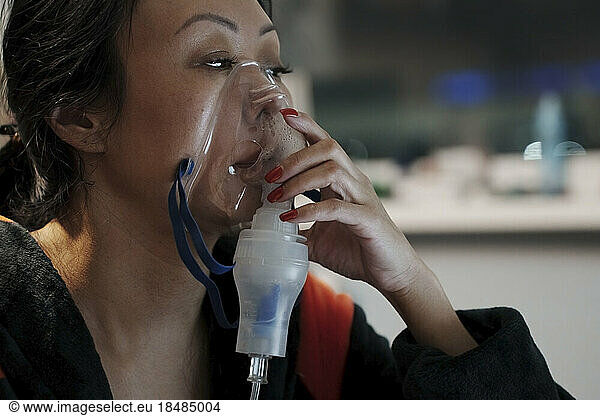 Woman inhaling through inhaler mask at home