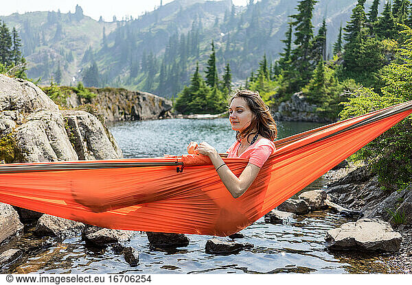 Woman is relaxing in a hammock at the alpine lake on local vacation