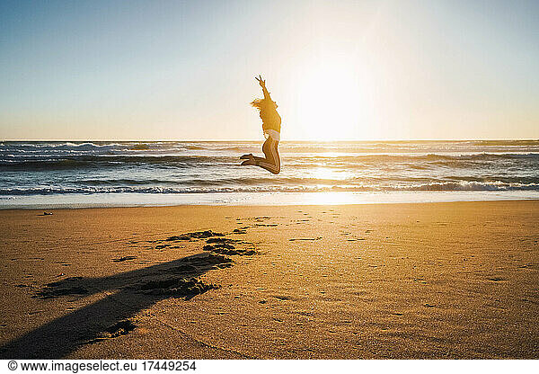 woman jumping on the shore of the beach at sunset