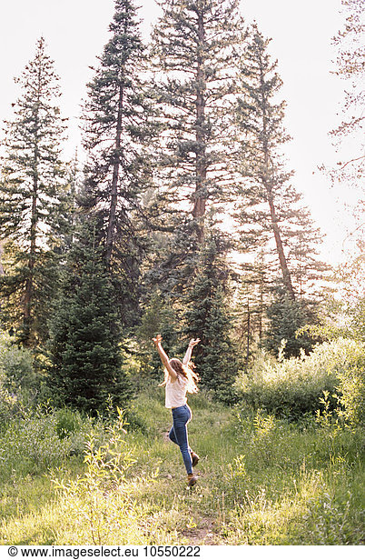 Woman jumping with joy in a sunlit forest.