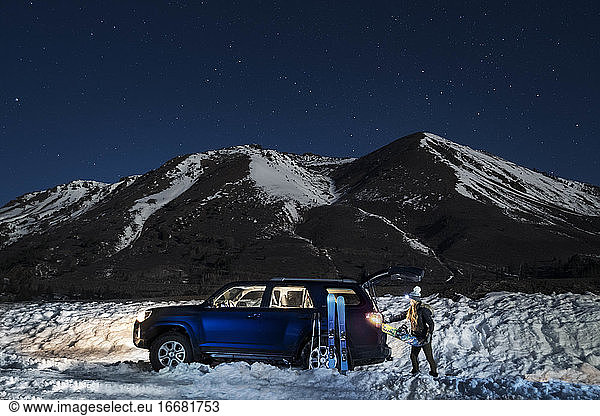 Woman keeping snowboard in trunk of car on snow covered land at night