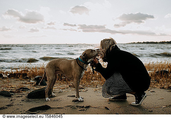 woman kissing her dog on the beach in the wintertime