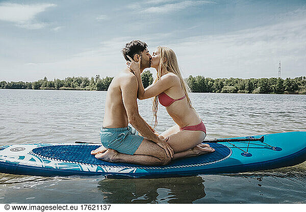 Woman kissing man sitting on paddleboard floating over lake