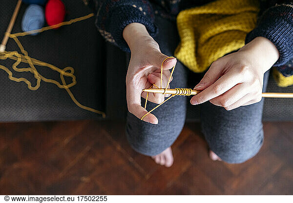 Woman knitting wool on sofa at home
