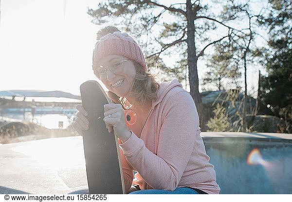 woman laughing holding her skateboard in a skatepark at sunset